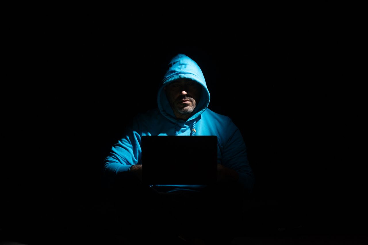 our-story-02 A person in a hoodie using a laptop in a dark setting, conveying mystery and technology themes.